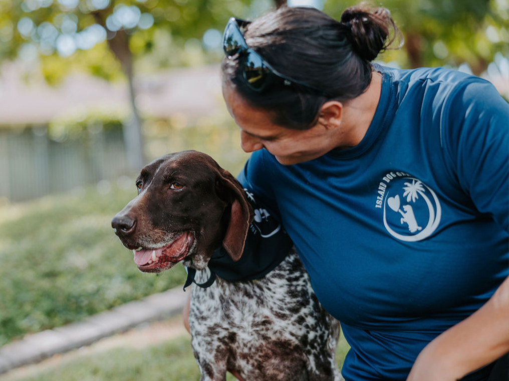 Oahu dog trainer smiling and bonding with a happy brown and white German Shorthaired Pointer during a personalized training session at Island Dog Obedience in a park.